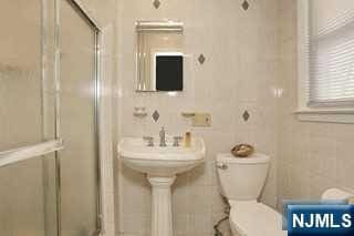 bathroom featuring toilet, a shower with shower door, and tile walls