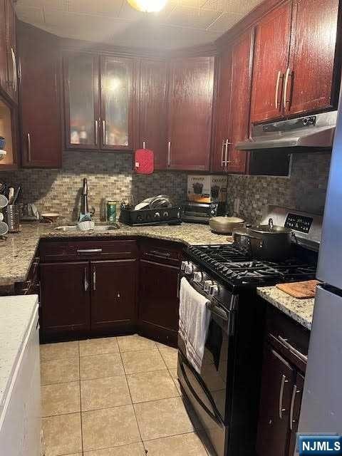 kitchen featuring sink, light stone counters, decorative backsplash, light tile patterned flooring, and appliances with stainless steel finishes