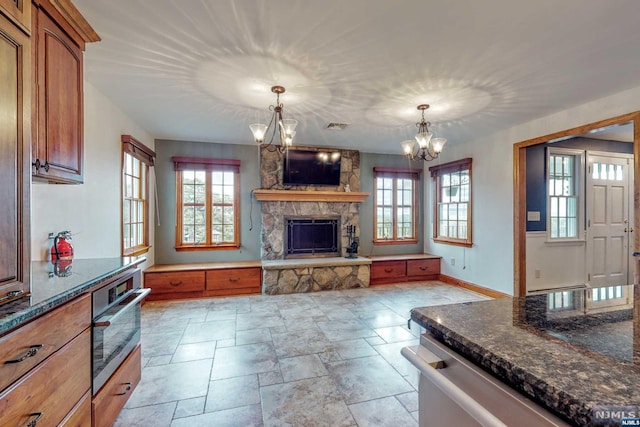 kitchen featuring pendant lighting, dishwasher, dark stone counters, a stone fireplace, and a chandelier