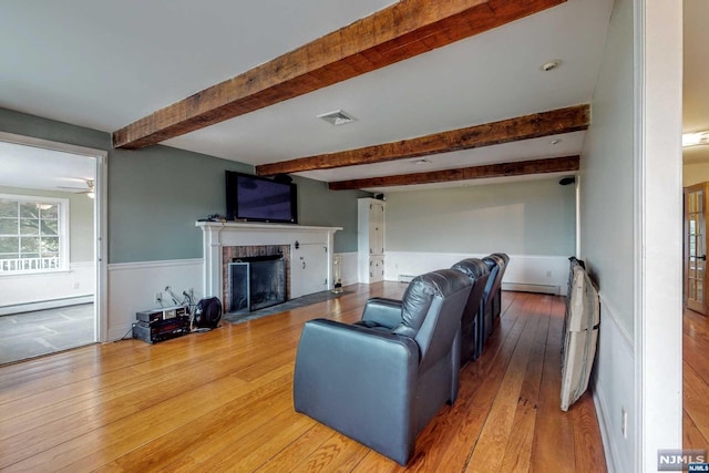 living room featuring ceiling fan, a brick fireplace, beamed ceiling, a baseboard heating unit, and hardwood / wood-style floors