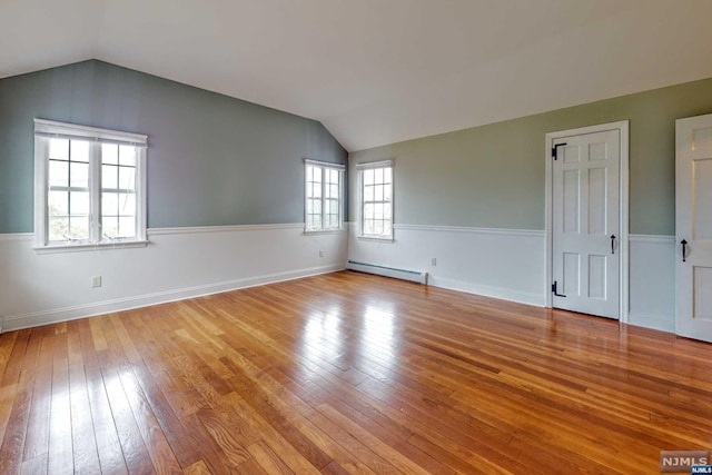 spare room featuring a healthy amount of sunlight, a baseboard radiator, vaulted ceiling, and light wood-type flooring