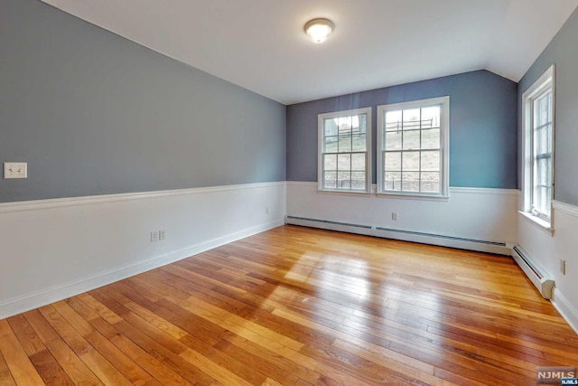 empty room with a baseboard heating unit, lofted ceiling, and light wood-type flooring