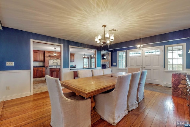 dining space with sink, a baseboard radiator, a stone fireplace, light hardwood / wood-style flooring, and a notable chandelier