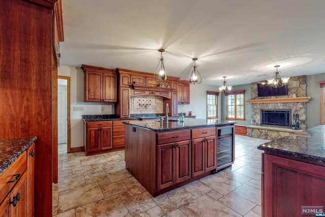 kitchen with wine cooler, a stone fireplace, a notable chandelier, decorative light fixtures, and a center island with sink