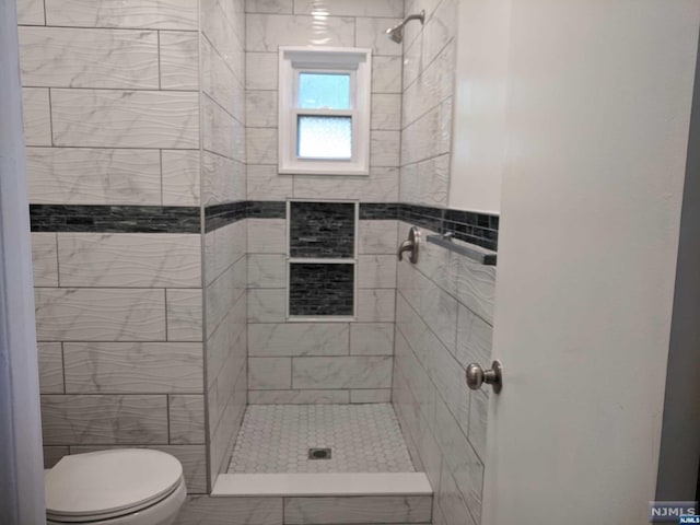 bathroom with a tile shower and toilet