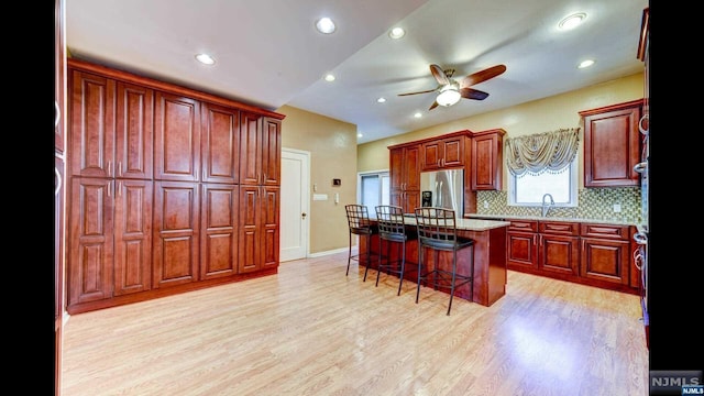 kitchen featuring tasteful backsplash, stainless steel fridge with ice dispenser, light hardwood / wood-style flooring, a breakfast bar area, and a center island with sink