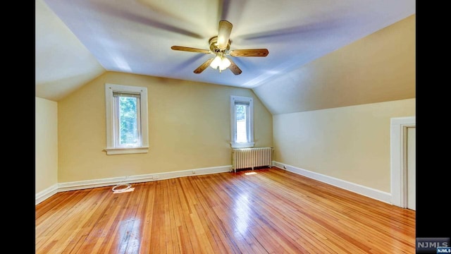 additional living space with a wealth of natural light, radiator heating unit, vaulted ceiling, and light hardwood / wood-style flooring