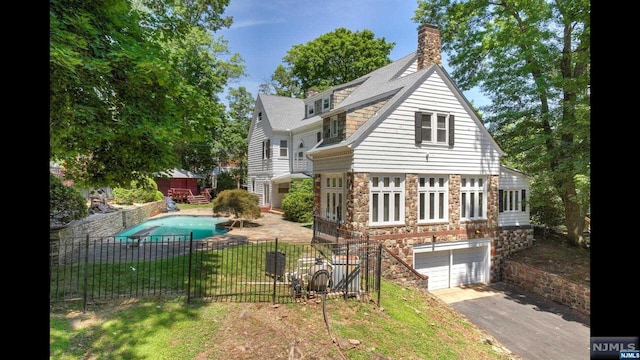 back of property with a fenced in pool and a garage