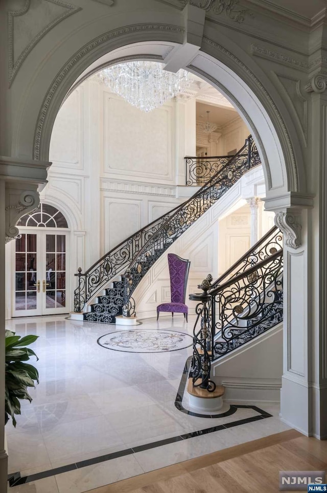 stairway featuring french doors, ornate columns, ornamental molding, a chandelier, and hardwood / wood-style floors