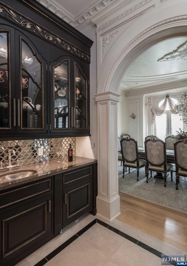 bar featuring tasteful backsplash, ornamental molding, light hardwood / wood-style flooring, and decorative columns