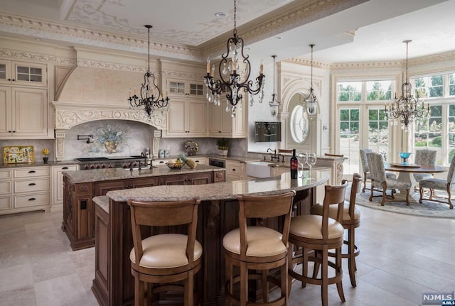 kitchen featuring a kitchen bar, light stone counters, a center island with sink, cream cabinetry, and hanging light fixtures