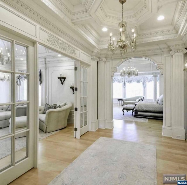 interior space with light wood-type flooring, coffered ceiling, and ornamental molding