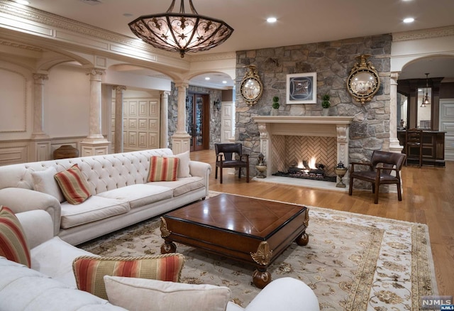 living room with a fireplace, ornamental molding, light hardwood / wood-style flooring, and decorative columns