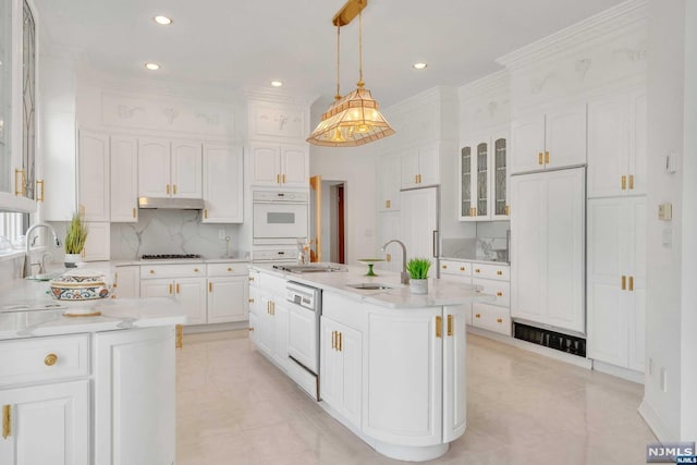 kitchen featuring white appliances, a kitchen island with sink, white cabinets, sink, and hanging light fixtures