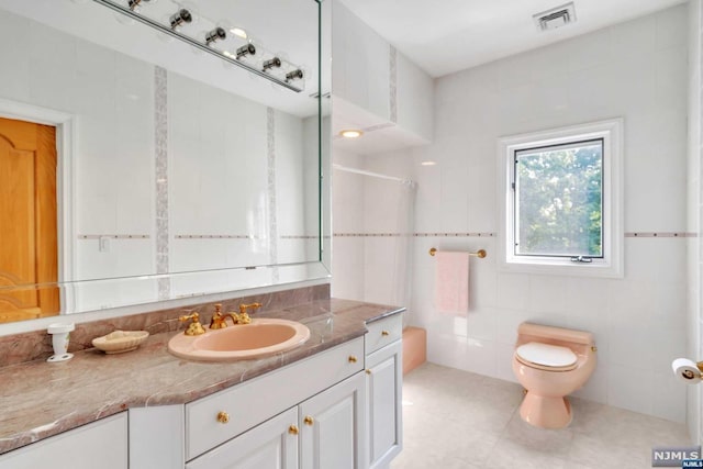 bathroom featuring walk in shower, tile patterned floors, toilet, vanity, and tile walls