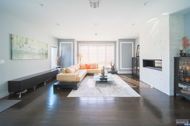 living room featuring a stone fireplace and dark hardwood / wood-style flooring