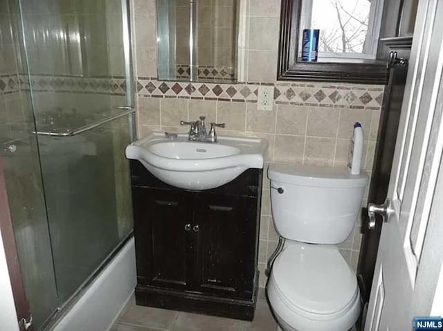 full bathroom featuring vanity, enclosed tub / shower combo, tile walls, and toilet