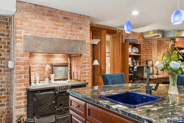 kitchen featuring pendant lighting, sink, brick wall, and dark stone counters