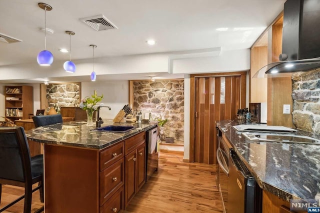 kitchen featuring wall chimney range hood, sink, hanging light fixtures, light hardwood / wood-style flooring, and a kitchen bar