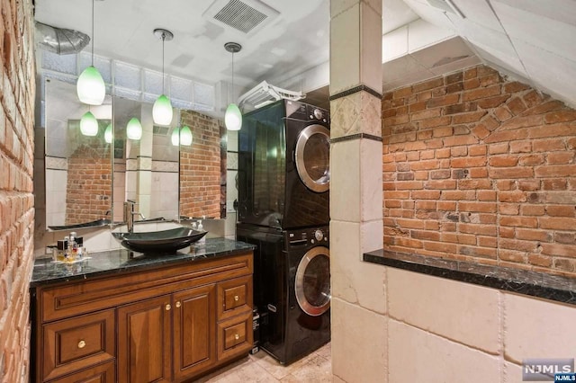 bathroom featuring stacked washer / dryer, vanity, and brick wall