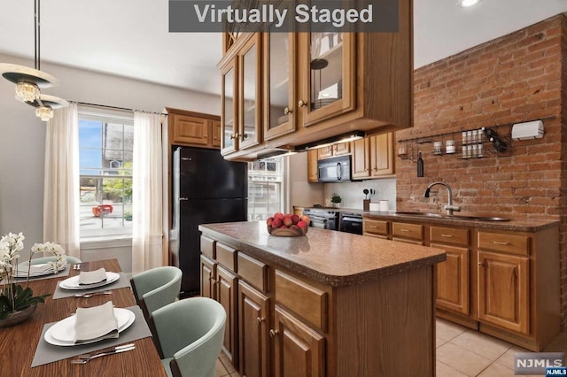 kitchen featuring a center island, black appliances, sink, light tile patterned flooring, and brick wall