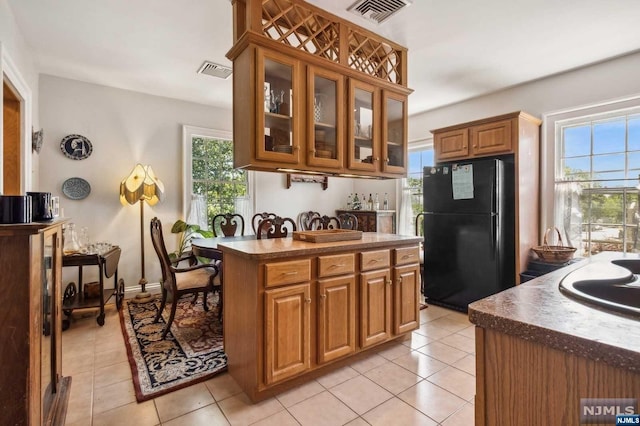 kitchen with black refrigerator, light tile patterned flooring, and a wealth of natural light