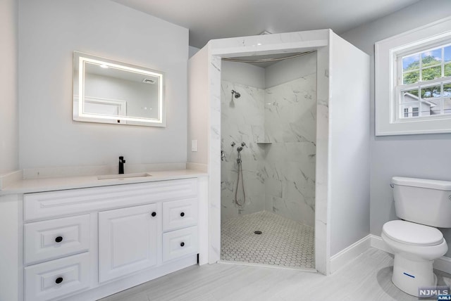 bathroom featuring hardwood / wood-style flooring, vanity, toilet, and tiled shower