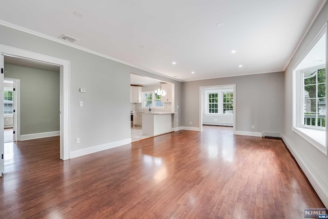 unfurnished living room featuring baseboard heating, crown molding, sink, wood-type flooring, and a notable chandelier