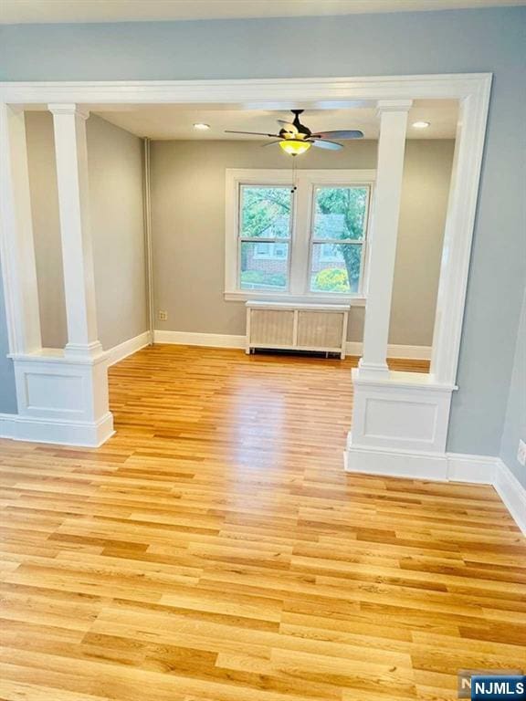 spare room featuring ornate columns, radiator heating unit, ceiling fan, and light hardwood / wood-style flooring