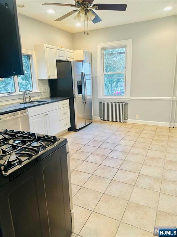 821 Roosevelt Ave, Secaucus, NJ 07094 - kitchen featuring radiator, light tile patterned floors, sink, white cabinetry, and stainless steel appliances