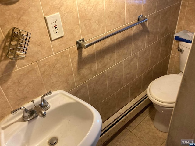 bathroom featuring sink, baseboard heating, tile patterned floors, toilet, and tile walls