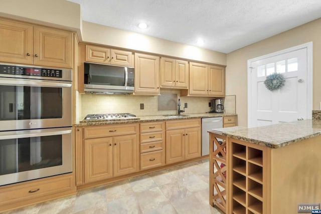 kitchen with light brown cabinets, light stone counters, sink, and appliances with stainless steel finishes