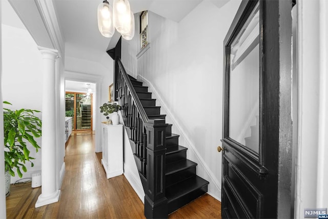 staircase featuring a notable chandelier, wood-type flooring, and ornate columns