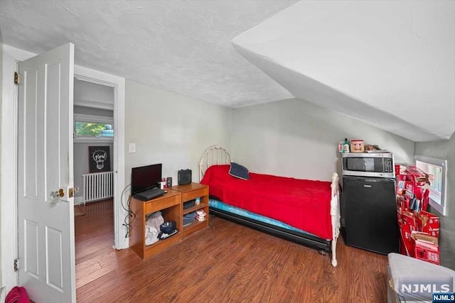 bedroom featuring dark wood-type flooring, black fridge, vaulted ceiling, a textured ceiling, and radiator heating unit