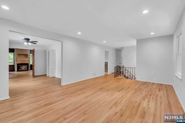 empty room with a fireplace, light wood-type flooring, and ceiling fan