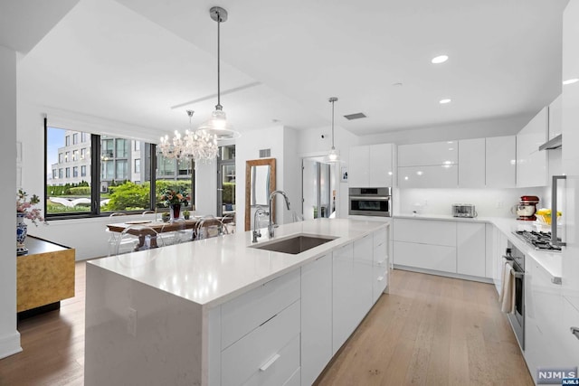 kitchen featuring pendant lighting, white cabinets, sink, an island with sink, and stainless steel appliances