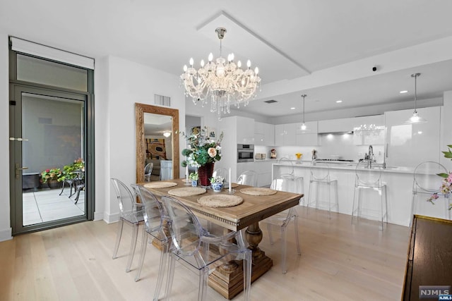 dining space with light hardwood / wood-style floors, an inviting chandelier, and sink