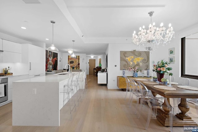 kitchen with white cabinets, pendant lighting, light hardwood / wood-style floors, and an island with sink