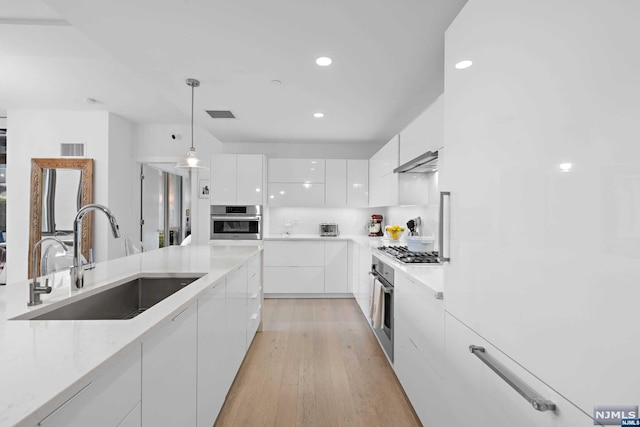 kitchen featuring white cabinetry, sink, pendant lighting, light wood-type flooring, and appliances with stainless steel finishes