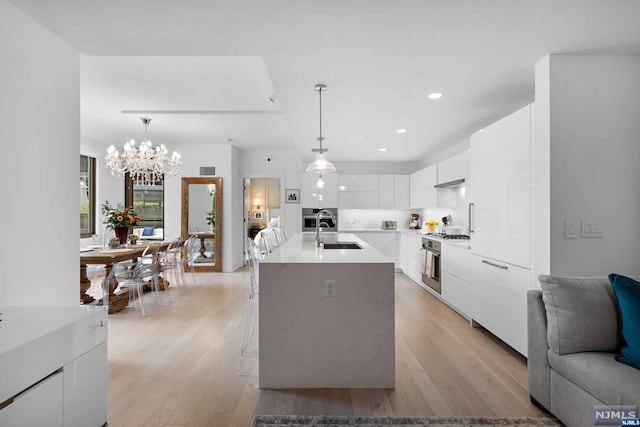 kitchen featuring white cabinetry, light hardwood / wood-style flooring, an island with sink, and pendant lighting