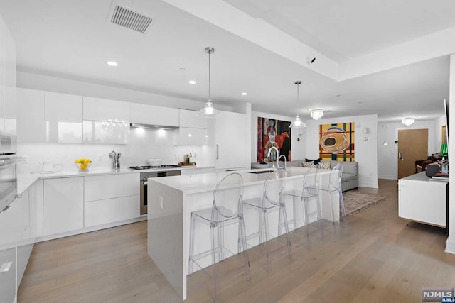 kitchen with white cabinets, decorative light fixtures, a kitchen island with sink, and light hardwood / wood-style floors