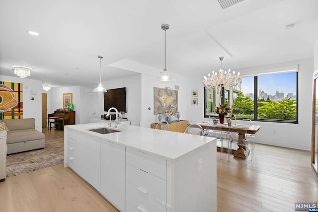 kitchen with sink, pendant lighting, a center island with sink, light hardwood / wood-style flooring, and white cabinetry