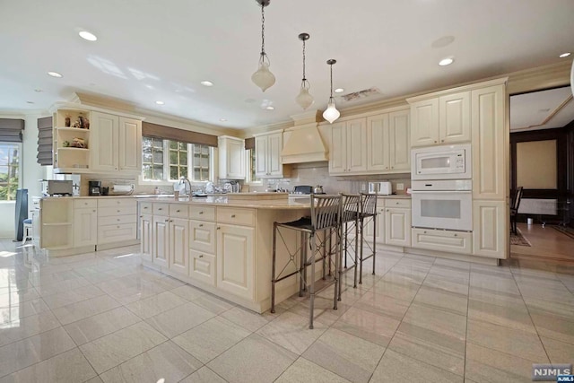 kitchen featuring custom range hood, white appliances, a kitchen island, hanging light fixtures, and a breakfast bar area