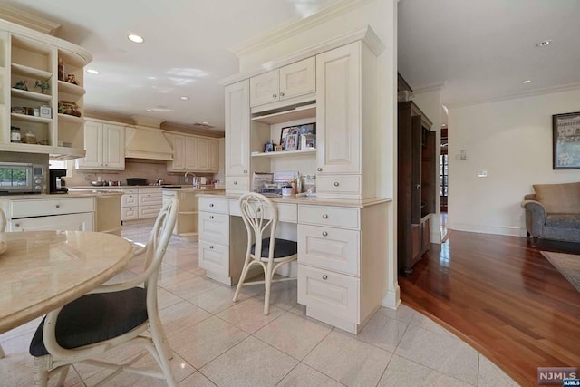 kitchen featuring custom exhaust hood, backsplash, crown molding, light wood-type flooring, and light stone counters