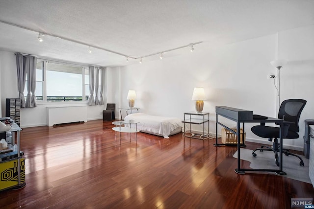 bedroom with a textured ceiling, wood-type flooring, rail lighting, and radiator