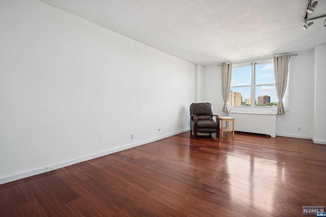 unfurnished room featuring a textured ceiling, rail lighting, and dark wood-type flooring