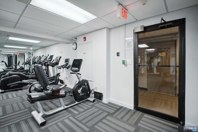 exercise room with a paneled ceiling and dark colored carpet