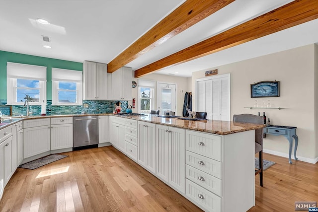 kitchen featuring white cabinetry, stainless steel dishwasher, kitchen peninsula, dark stone countertops, and light hardwood / wood-style floors