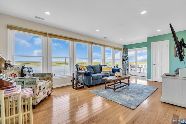 living room with light wood-type flooring, a water view, and a healthy amount of sunlight