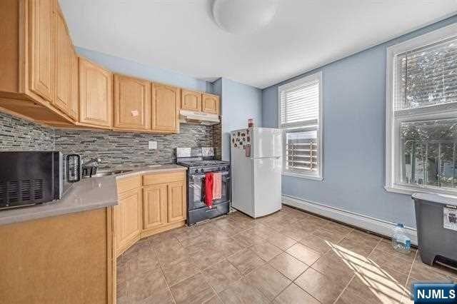 kitchen featuring white refrigerator, black range with gas stovetop, sink, decorative backsplash, and light brown cabinetry